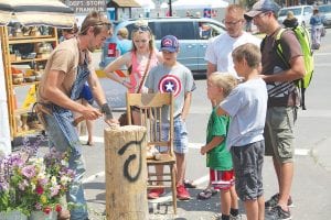 The 25th Grand Marais Arts Festival on July 11-12 offered many opportunities to see artists in action. Right: Tim Dennison of Grand Marais enthralls a group with his hatchet skills. Below: The Grand Marais Art Colony booth offers hands-on activities for kids of all ages. These girls enjoyed working with clay.