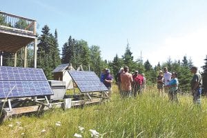 An interested group of 10-14 people ask Luke Gulstrand questions about his solar PV system. His family of four live comfortably with the stand-alone system they have developed. The tour included the panels, the battery area, and descriptions about how they use (or not use) electricity throughout the day and night.