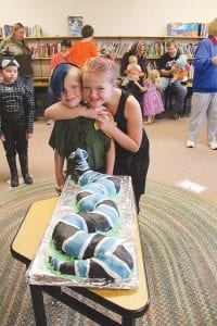 Above left: The community brought dozens of colorful and creative cakes for the Cake Walk. Most coveted was the snake cake made by Michaela Schliep. The lucky winner was “Peter Pan” (Carson) with his very happy sister, Delilah Kindstrand. Above right: Justin won a pretty princess cake and he gave it to Halloween princess Brookston!