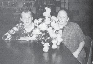 The local chapter of the Salvation Army continued its tradition of placing Christmas trees in area banks and the credit union in December 1996. The trees are decorated with angels, each handmade and accompanied by a description of a child in need; citizens are then encouraged to take an angel and return with gifts for that child. Shown are Ashley Smith and Miranda Clark, two of the students who made angels for the trees, with one of their creations.