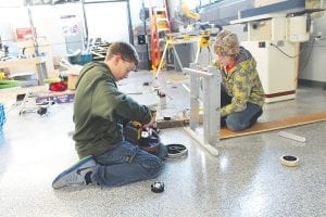 John VanderHeiden (right) and a visiting friend make precise adjustments to the wheels that spin to provide momentum to toss the ball into the “tower” on the Stronghold obstacle course.