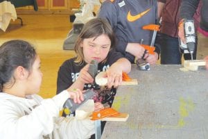 Above: These two third graders worked together to shave down the canoes, watching and chatting to see how the other was doing. Left: With instructor Peter Barsness’s help, the two kids and mom mark the sections of the tiny canoes to shave off.