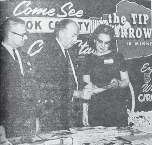 George Kratoska, executive secretary of the Cook County Civic Council, traveled with his wife to the Chicago Sports Show, where he reported huge crowds. “It is an indication that people will be vacationing, especially in this area,” Kratoska said of the event, where he distributed 15,000 “Tip of the Arrowhead” maps along with hundreds of individual pamphlets about Cook County resorts and places of interest. Gov. Karl Rolvaag, center, is shown looking over one of the publicity folders at the March 1966 event with Mr. and Mrs. Kratoska.