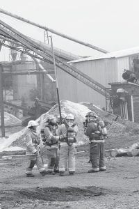 Firefighters in turnout gear prepare to enter the smoke-filled sawmill at Hedstrom Lumber Company on Wednesday, June 8. In addition to hoses, firefighters used a pike pole to probe wall and ceiling spaces, looking for places where the fire may have spread.