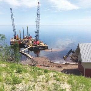 At the beginning of June, two barge derricks arrived at the beach west of Lutsen Resort to work on the Lake Superior- Poplar River Water District pipeline. Roen Salvage of Sturgeon Bay, Wisconsin blasted and dug a 4-foot deep trench from the shoreline to 350 feet out into the lake. The water line pipe was placed in the trench and then covered with cement pumped down from the top of the hill to the derricks. A team of divers worked under water, directing and finishing the concrete. Roen Salvage finished the job on June 27.