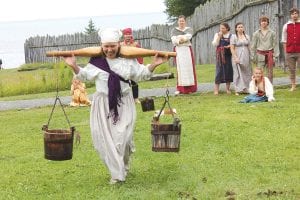 The Dainty Voyageur competitors must do “women’s work”—haul water, kill an attacking “beaver,” sweep out the camp tent and button a gentleman’s jacket all while carrying a baby on their back. Left: Justine takes on the “rabid beaver” with a cast iron frying pan. Above: Hauling water is likely one of the most difficult tasks in the Dainty Voyageur contest, but Judy made it look fairly easy.