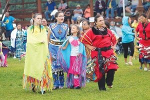 Left: Clouds threatened, but the rain held off until after the Saturday, August 13 Rendezvous Days Powwow Grand Entry and flag-raising ceremonies. Despite the rain, the dancers stayed in the arena. Middle: Autumn Clearwater Day of Grand Portage was among the dancers. Right: This dancer had a unique staff fashioned of diamond willow and a deer antler.