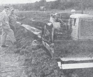 Work was under way on a new football field at Cook County High School when this photo was taken in October 1960. The plans for the new field were based on those used at Wisconsin State College at Superior, at a cost of $10,000. The old field was 4½ feet higher at one end than at the other and kept pushing up sharp volcanic rock, which actually made it dangerous to play on. Shown looking over the progress are Cat driver Tom Allard and high school principal Leonard Sobanja.