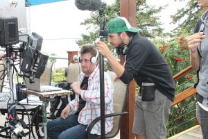 Rushaway Pictures is shooting scenes for its feature film, Virginia, Minnesota along the North Shore. The production company has been in Grand Marais all week, filming at World’s Best Donuts, on the Grand Marais waterfront, on Wisconsin Street and here, on the rooftop of the GunFlint Tavern. Microphone boom operator Christian Cole and script supervisor Andrew Bjorklund look at the next scene to determine how wide the shot will be.