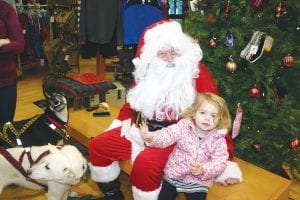 Wide-eyed, excited Isla Arhelger, age 3, traveled a long way to meet Santa Claus. Isla, seen here waving at the world, and her parents came from Minneapolis to greet the friendly, bubbly white-bearded bequeather of Christmas presents. Santa and his two snow dog helpers were very busy meeting children at Stone Harbor last Friday night right before the annual Christmas Parade. Rudolph, Dancer, Prancer and the rest of the reindeer couldn’t fit inside the store. They were outside in the back taking a much-deserved nap.