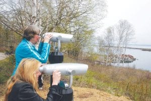 Cook County Commissioner Ginny Storlie (standing) and Visit Cook County representative Anna Klobuchar look through the new viewfinders at the Taconite Harbor following the ribbon-cutting ceremony.