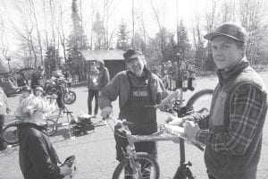 Above: He might have sold his bike shop, but Mark Spinler (hands on bike) still volunteers to fix bikes for free at the bike rodeo. Clipboard in hand, Henry DeArruda Weaver keeps track of what has been fixed. Left: One hand in his pocket, one hand shading the sun, Bo Christianson watches intently as Jay Arrowsmith DeCoux strives to improve Bo’s bike to make it a smooth ride.