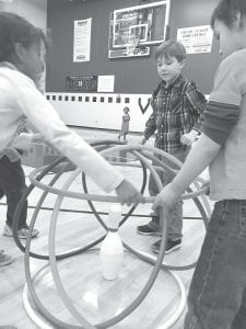 Scarlet Higgins (right), Alex Teeter, and Wyatt Dahl put the roof on their hula-hoop castle. “Castle Ball” involves using offensive and defensive strategy to protect your king and queen (bowling pins) in their castles while trying to knock over the other team’s castles and royalty.