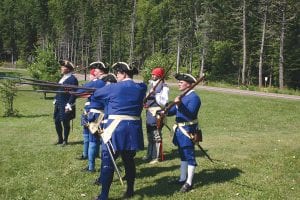 Above: La Compagnie de La Vérendrye, a re-enacting group of colonial French militia based out of Winnipeg, performed drills for the audience on hand. Left: Paul Cummings makes a paddle using a hatchet.