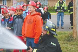 Above: Although there was a variety of firefighting activities on display on Friday, October 13, the kids gravitated to spraying water from the high-pressure hoses, as this line of children demonstrates. Right: Louise Trachta helps this potential little glee-filled firefighter aim water at the brush and tall grass by Birch Grove Community School.