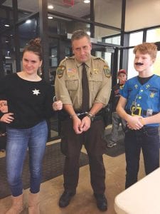 Cook County Sheriff Pat Eliasen looks distraught as Aurora Schelmeske and Jack Willis handcuff him. Top: Cook County Community YMCA Director Emily Marshall had a whole crew of young deputies arrest her during the recent Youth in Government fundraiser held at the Y.