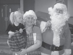 Above: The residents were treated to a visit from this cute little elf, Mrs. Claus, and Santa on Christmas Eve. Left: Santa had plenty of help distributing gifts to the residents at the Care Center. Pictured here is three-year-old Euell Oksness presenting a gift to Mary Liebsch.