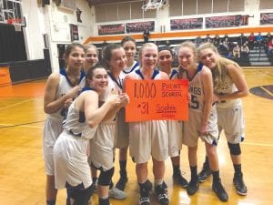 Surrounded by her jubilant teammates, Vikings’ junior guard Sophie Eliasen smiles broadly as she holds up the cardboard banner showing she went over the 1,000-point barrier. Eliasen achieved the milestone in the game against the Wrenshall Wrens.