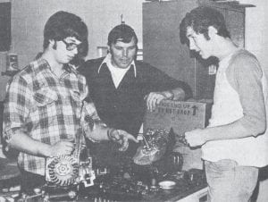 Cook County High School industrial arts teacher Chuck Beberg looks on as Scott Bystrom, left, and Doug Schinn tackle the task of disassembling two Briggs & Stratton four-cycle engines. Thirty students (three of them girls) participated in the new vocationally-oriented small engines class that was offered in 1979 with the financial assistance of the Minnesota Department of Education-Vocational Education Division. Students had to take apart and put back together a lawn mower engine, as seen here, or could bring in their own small engines to work on; snowmobile engine work seemed to be the most popular.