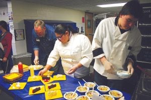 The high school culinary arts program contributed to the EATS event with some tasty treats. From left: Culinary arts teacher Jason Gesch along with students Alize Pierre and Cedric Rock work fast to make sure the table was full of food throughout the evening.