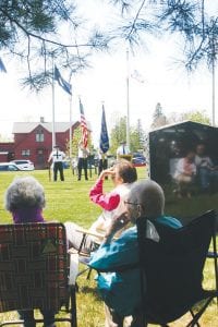 With the Honor Guard standing at attention in the distance, Bernice Howard, age 94, her hand sheltering her vision from the sun, looks at the Memorial Day speaker Kris Hoffman (not pictured) with Eleanor Waha, age 95, seated directly behind her. The two women were part of a crowd of about 100 people who took part in the Memorial Day remembrance at the courthouse lawn.